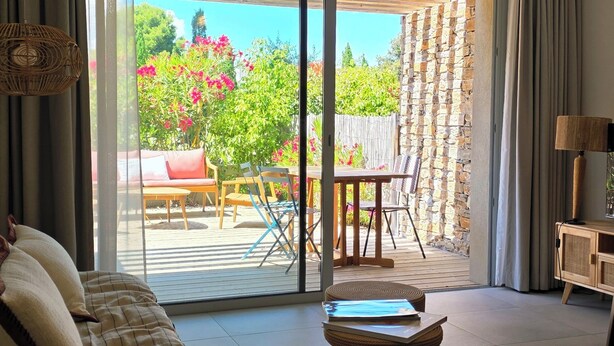 Una sala de estar con sofá, una mesa de centro y vistas al exterior a través de una puerta corrediza de vidrio.