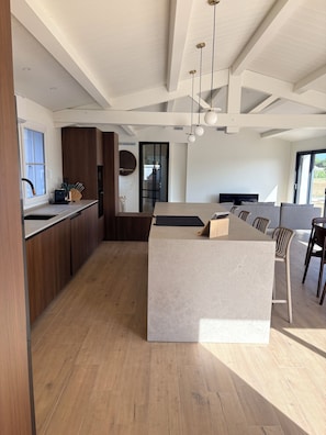 A modern kitchen with a central island, wooden cabinets, and a dining area with chairs. - Doudou House. Exceptional family home with swimming pool in Oléron (Saint-Denis-d'Oléron)