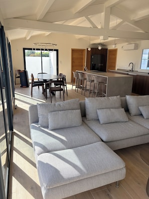 A modern living room with a sectional sofa, a dining area, and a kitchen with a bar. - Doudou House. Exceptional family home with swimming pool in Oléron (Saint-Denis-d'Oléron)