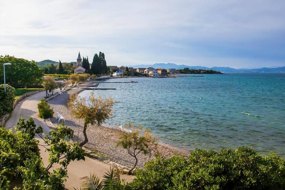 A coastal area with a paved walkway, a church, and residential buildings along the water.