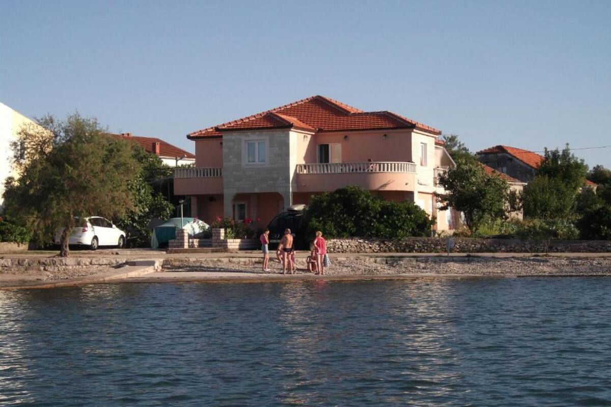 A coastal building with a red-tiled roof, a stone facade, and a balcony.