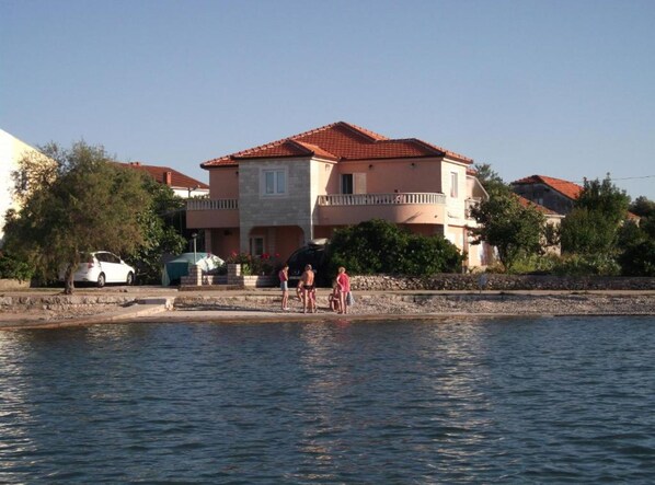 Um edifício costeiro com telhado de telhas vermelhas, fachada de pedra e varanda.