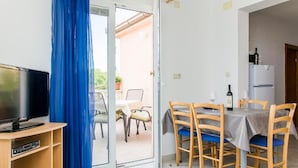 A room with a TV, a dining table with chairs, a refrigerator, and a blue curtain. - Apartments Sea View Pelješac (Janjina)
