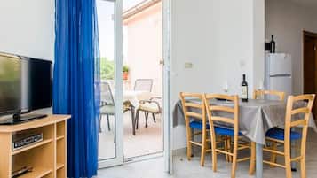 Een kamer met een televisie, een eettafel met stoelen, een koelkast en een blauw gordijn.