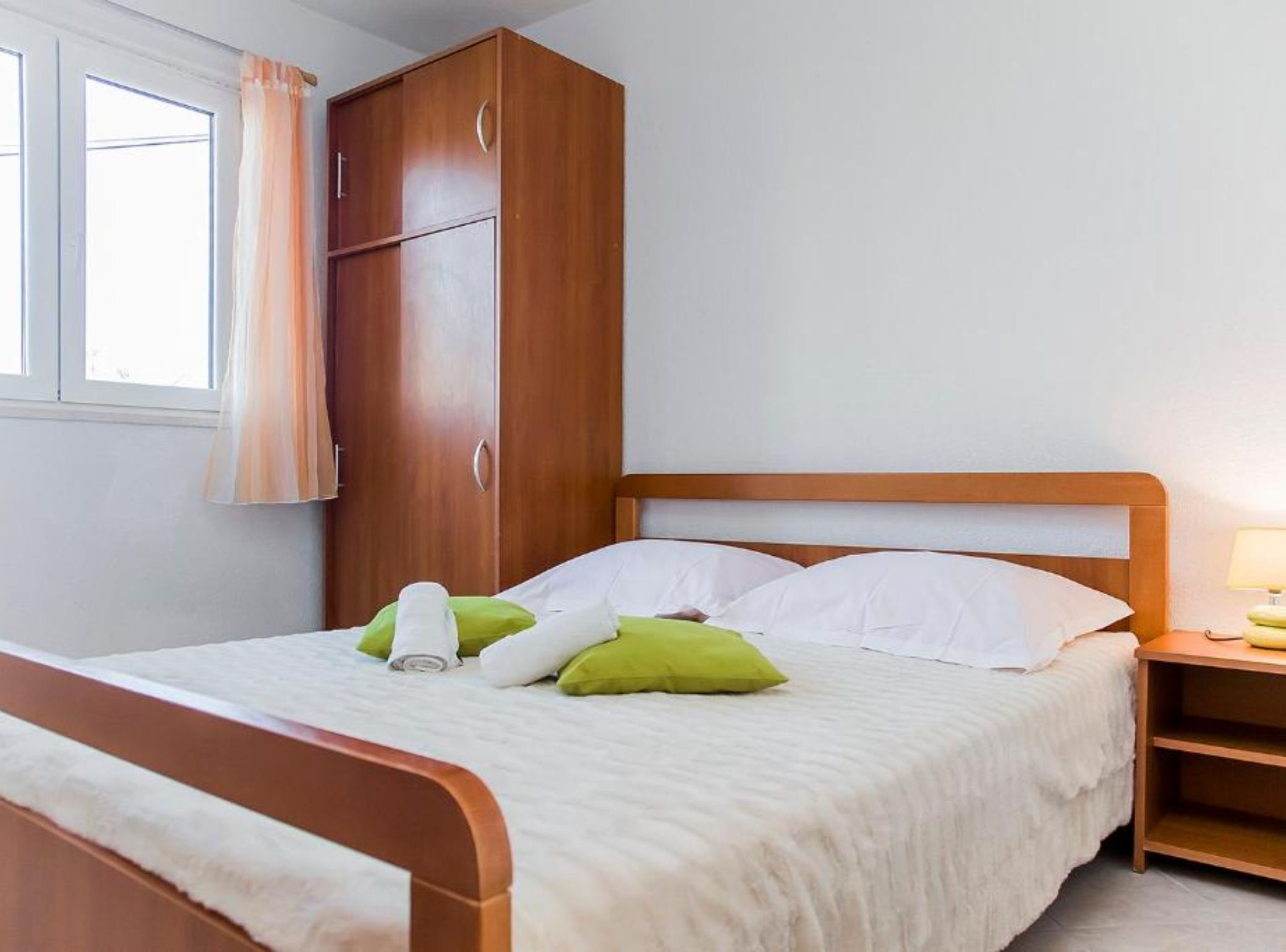 Ein ordentlich bezogenes Bett mit weißen und grünen Kissen, einem Holz-Kopfstück und einem Schrank aus Holz mit Griff.
