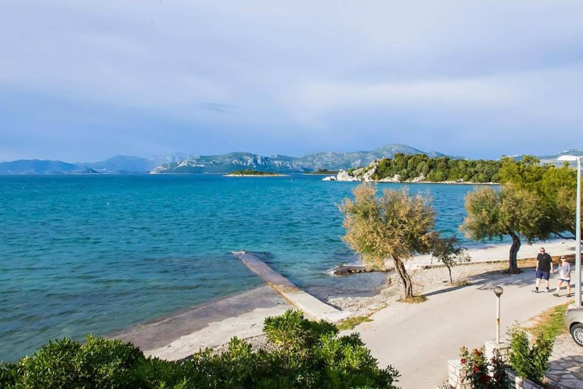 A coastal view with a clear sky, calm sea, and a sandy beach with a few people.