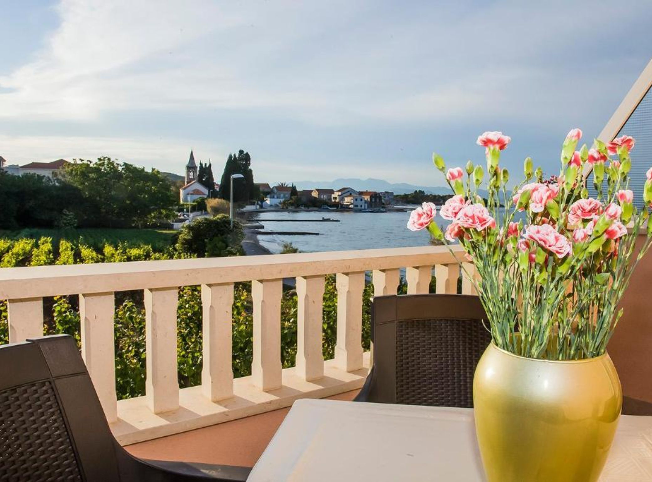 Een balkon met uitzicht op een rivier, een bloevas en een tafel met stoelen.