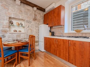 A kitchen with wooden cabinets, a white refrigerator, a dining table with blue chairs, and a stone wall. - Apartments Nonna (Komiza)