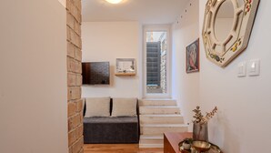 A hallway with a wooden floor, a sofa, a staircase, a wall-mounted mirror, and a small table with a plant. - Apartments Nonna (Komiza)