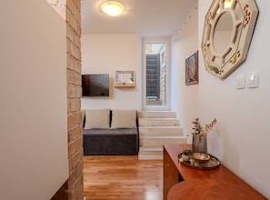 A hallway with a wooden floor, a sofa, a staircase, a wall-mounted mirror, and a small table with a plant. - Apartments Nonna (Komiza)