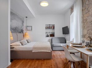 A modern bedroom with a bed, a sofa, a dining table with chairs, a bookshelf, and a TV. - Apartments Nonna (Komiza)