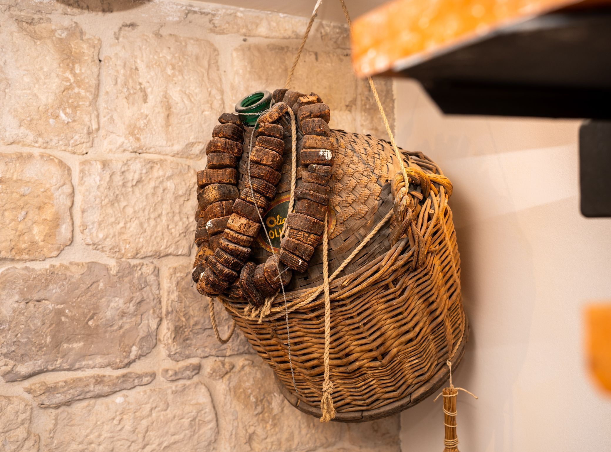 A wicker basket with a rope and a green object, hanging on a stone wall.