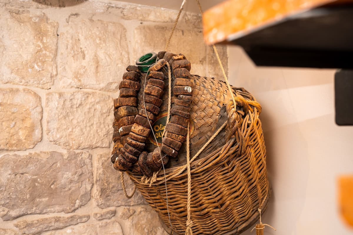 A wicker basket with a rope and a green object, hanging on a stone wall.