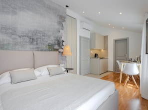 A modern bedroom with a large bed, bedside tables, a wall-mounted air conditioner, and a kitchenette in the background. - Apartments Nonna (Komiza)