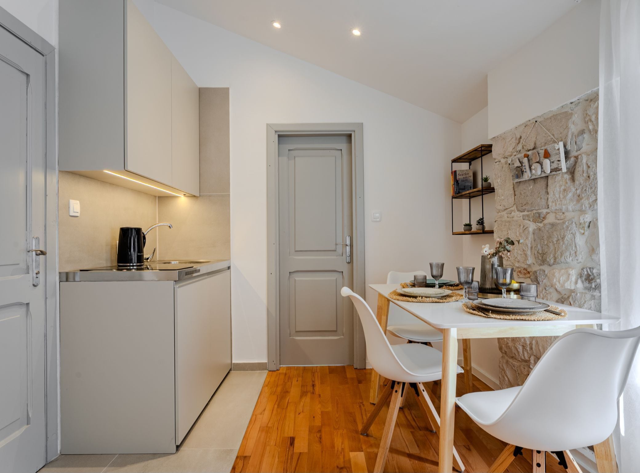 A compact kitchen with a coffee maker, a dining table with chairs, and a stone wall.