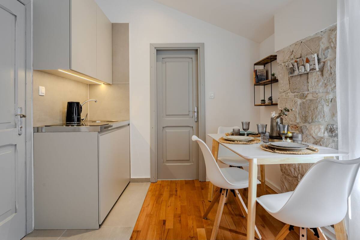 A compact kitchen with a coffee maker, a dining table with chairs, and a stone wall.