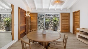 Et moderne spiseområde med et rundt træbord, polstrede stole og et loft med hvide bjælker.