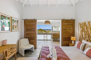 A bedroom with a bed, a chair, a desk, and a view of the beach through an open door. - Splendid sea view, close to beaches. (SAINT-MARTIN)