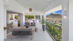Uma varanda espaçosa com vista para uma paisagem montanhosa, equipada com um sofá, cadeiras e uma mesa.
