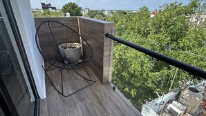 Ein Balkon mit Stuhl, Geländer und Blick auf Bäume und Gebäude.