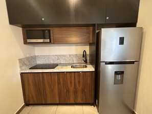 Uma cozinha compacta com micro-ondas, geladeira de aço inoxidável e pia.