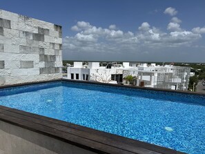Piscina no terraço com vista para edifícios e céu claro.
