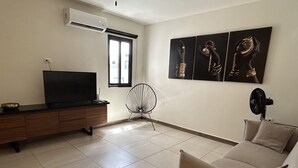 Ein Wohnzimmer mit Fernseher, Ventilator, Sofa und Kunstwerken an der Wand.