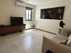 Uma sala de estar com televisão, ventoinha, sofá e obras de arte na parede.