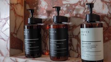 Tres botellas de acondicionador para cabello Olive Era sobre un estante de mármol.