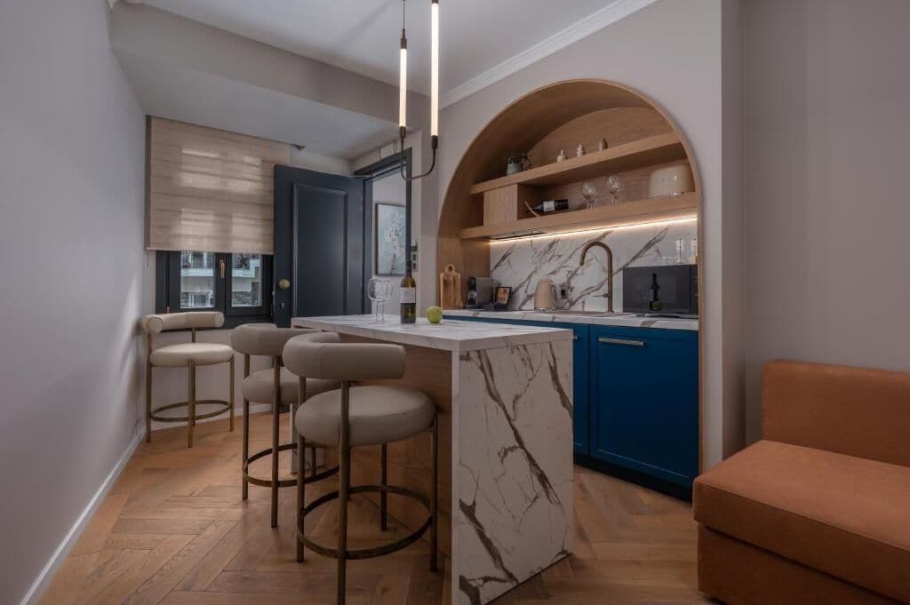 A compact kitchen with a marble island, bar stools, and a blue cabinet.