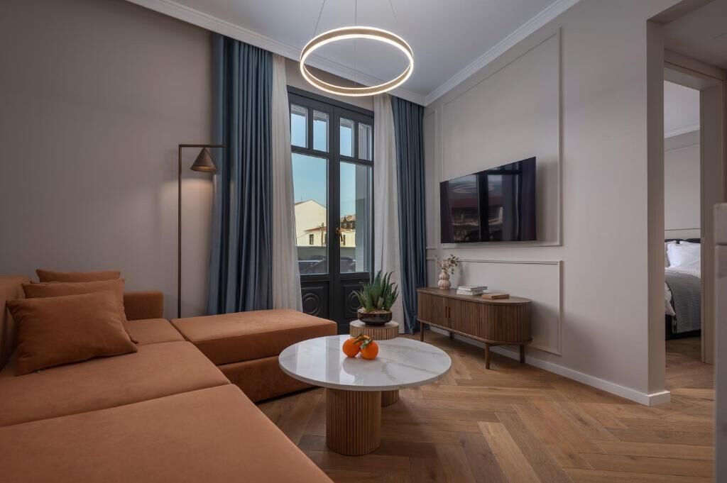 Un salon moderne avec un canapé, une table basse ronde, un téléviseur fixé au mur et une fenêtre avec des rideaux.