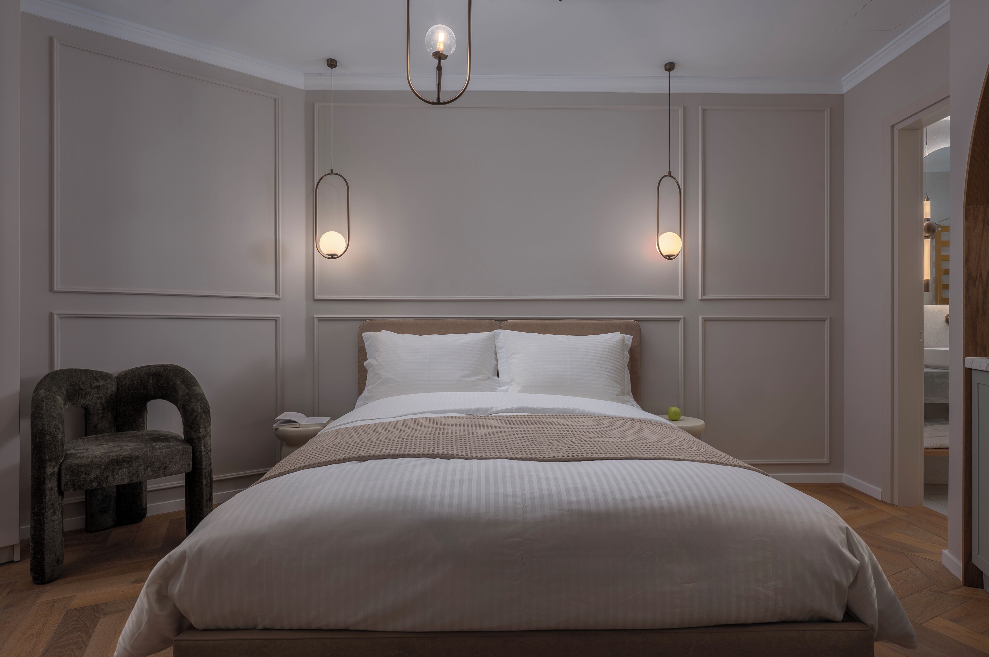 A bedroom with a large bed, two bedside tables, a chair, and pendant lighting.