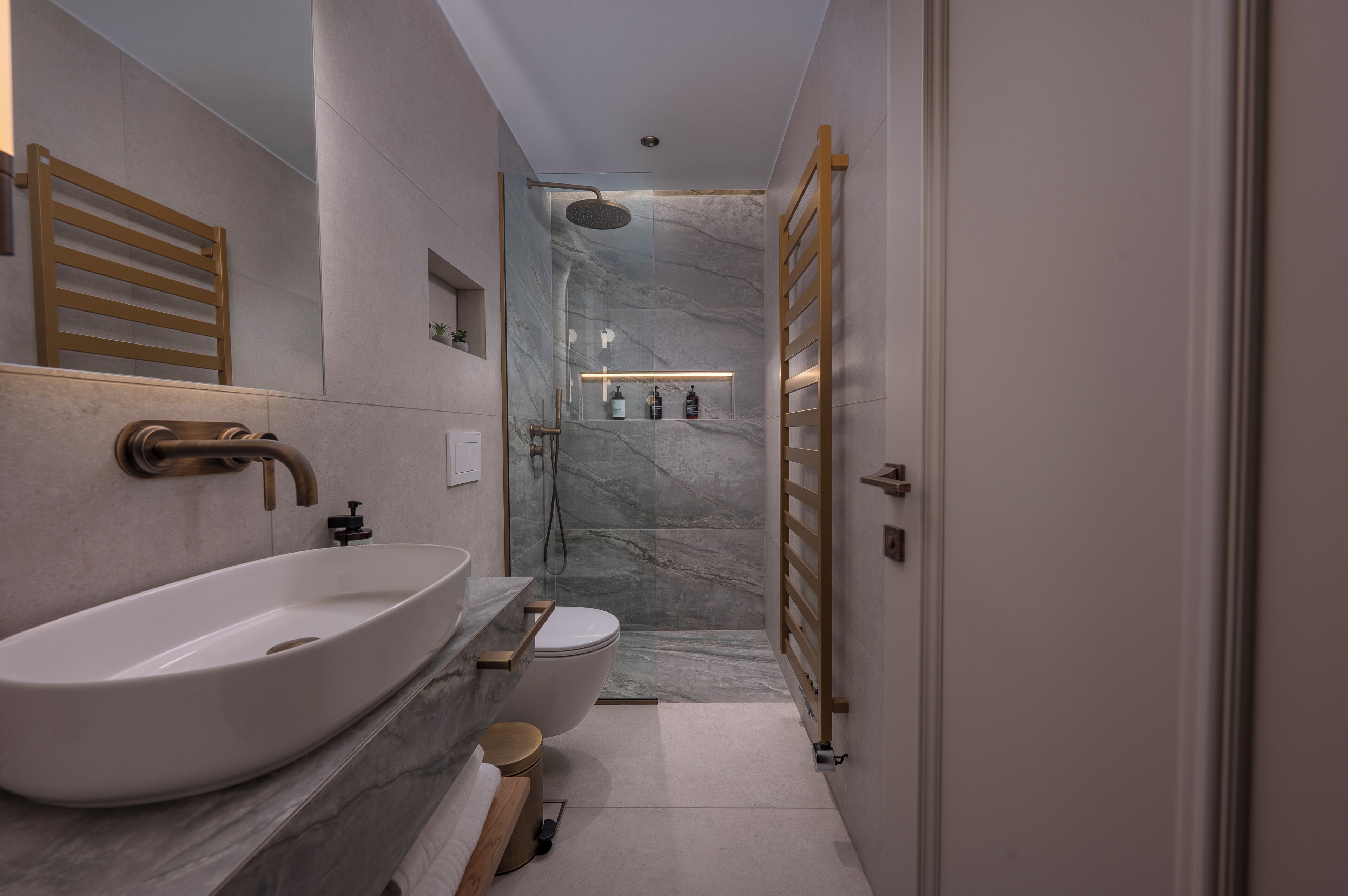 A modern bathroom with a large white sink, a toilet, a shower, and a wooden towel rack.