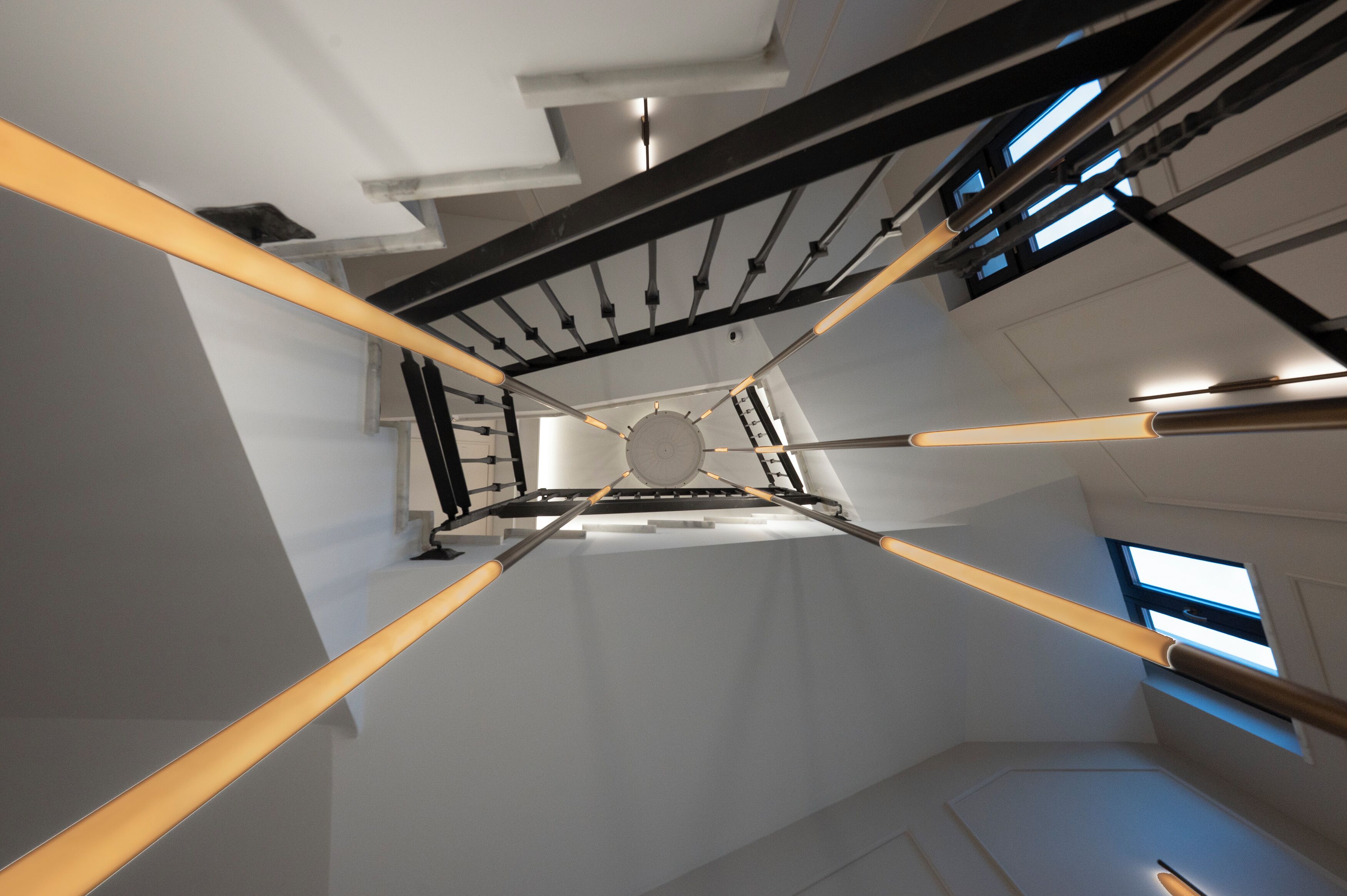 Un intérieur moderne avec un escalier central, des murs blancs et un plafond avec des poutres apparentes.