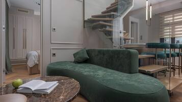 Un espacio de estar moderno con un sofá verde curvo, una mesa de centro de mármol y una escalera con barandillas de cristal.