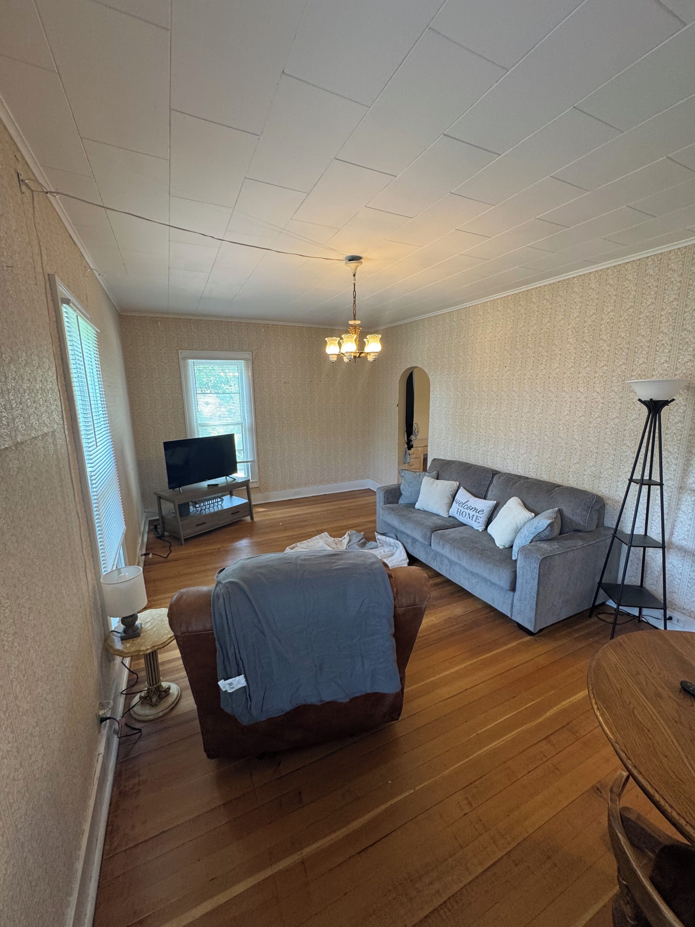 Un salon avec un canapé, un téléviseur, un lustre et une lampe sur pied.