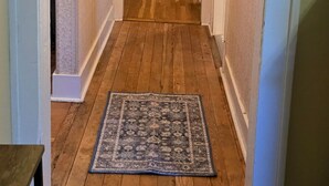 Un couloir avec un plancher en bois, un tapis, un bureau avec des tiroirs, une chaise et un lit.
