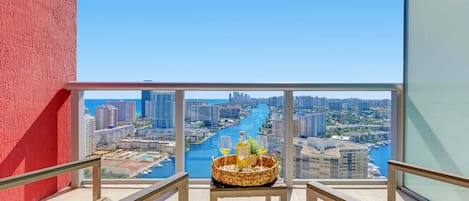 Ein Balkon mit Blick auf die Stadt, ein Tisch mit einer Snackauswahl und eine Flasche Alkohol.