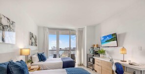 Ein modernes Hotelzimmer mit Bett, Nachttischen, Schreibtisch, Stuhl, Fernseher und einem großen Fenster mit Blick auf die Stadt.