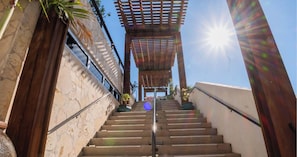 A staircase leading to a covered area with a pergola, surrounded by stone walls and plants. - High-Floor Retreat 2BR - Beachwalk Resort (Hallandale Beach)