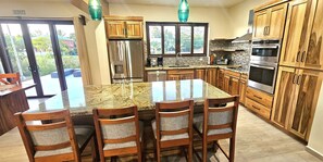 A kitchen with a large island, wooden cabinets, stainless steel appliances, and a view through the glass door. - Placencia Villa for 8 guests, Beach, Luxury, Pool (Placencia)