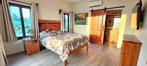 Ein Schlafzimmer mit Bett, Nachttisch, Schminktisch, einem Gemälde und einer Schiebetür zum Badezimmer.