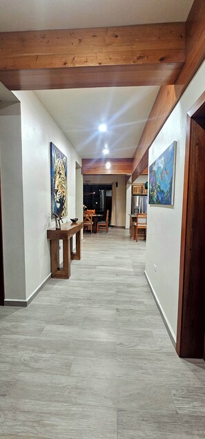 Un pasillo espacioso con vigas de madera, una zona de comedor con sillas y obras de arte en las paredes.
