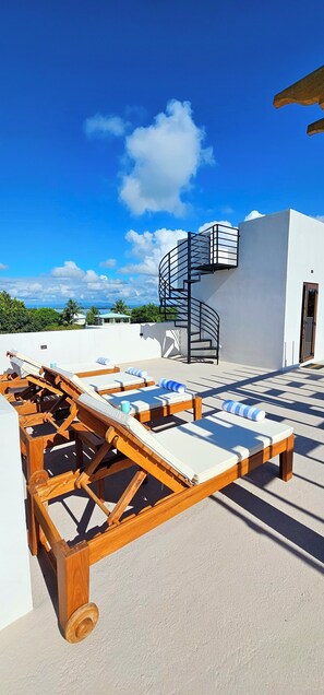 Eine Dachterrasse mit Liegestühlen, einer Wendeltreppe und Blick aufs Meer.