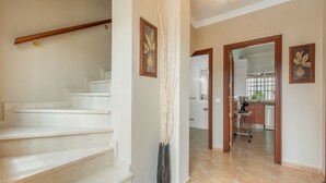 Eine Treppe führt zu einer Zwischenebene, eine Vase mit Zweigen und ein Küchenbereich mit Schränken und einem Geschirrspüler.