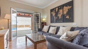 Ein Wohnzimmer mit grauem Sofa, einem Glastisch, einer Weltkarte an der Wand und einer Glastür, die zu einem Außenbereich führt.