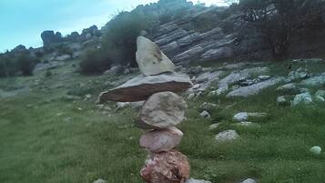 Una pila de piedras sobre un poste de madera en un campo cubierto de hierba, con una colina rocosa al fondo.