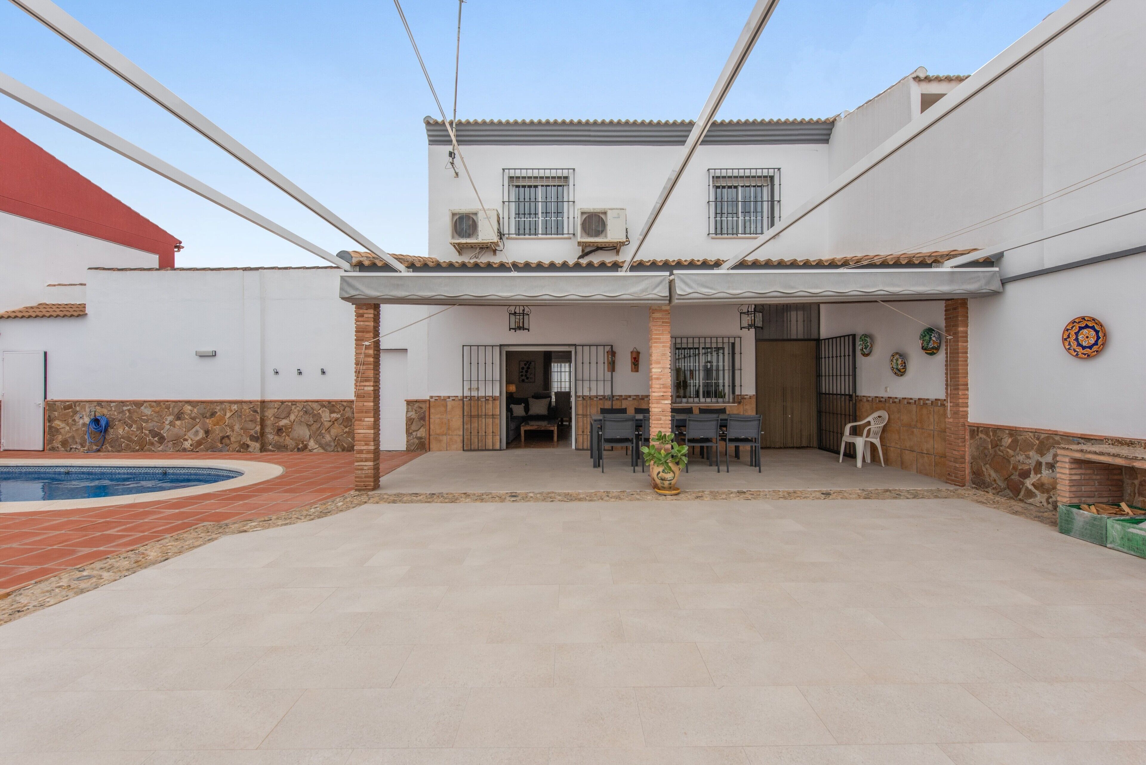 A covered patio area with a pool, outdoor seating, and a two-story building with a tiled roof.