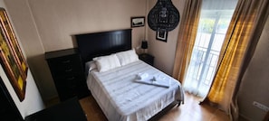 A hotel room with a bed, a nightstand, a lamp, a painting, and a window with curtains.
