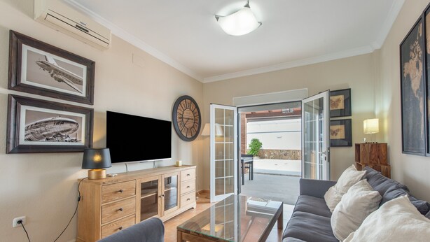 Ein Wohnzimmer mit einer Couch, einem Glastisch, einem Fernseher auf einer Holzkommode und einer Wanduhr.